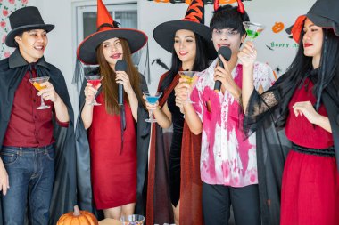 Kostüm giymiş genç Asyalı cadı çetesi, Cadılar Bayramı partisini kutlayan büyücü odada şarkı söyleyip içki içen büyücü. Gençler ve Taylandlılar Cadılar Bayramı 'nı kutluyor. Kavram partisi Cadılar Bayramı evde.