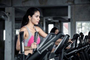 Asyalı genç kadınlar spor salonundaki egzersiz makinesinde gülümseyerek egzersiz yapıyorlar. Spor salonunda sağlık hizmeti ve egzersiz kavramı. Güzel kız spor salonunda spor yapıyor..