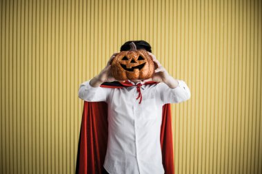 Cadılar Bayramı kostümü giymiş genç Asyalı adam kavramı ve sarı arka planda Cadılar Bayramı turuncu balkabağı.