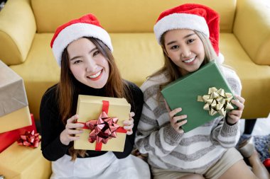 Genç Asyalı kadın ve kız arkadaşı hediye kutuları tutuyorlar ve Noel festivalinde mutlu bir gülümsemeyle birlikte eve bakıyorlar. İki güzel Taylandlı kız Noel 'i ve yeni yılı kutluyor.