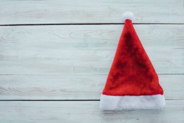 Noel Baba 'nın kırmızı Noel Baba şapkasıyla ahşap arka plan ve fotokopi alanının üst görüntüsü. Noel aksesuarları ve yeni yıl konsepti.