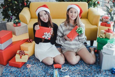 Genç Asyalı kadın ve kız arkadaşı hediye kutuları tutuyorlar ve Noel festivalinde mutlu bir gülümsemeyle birlikte eve bakıyorlar. İki güzel Taylandlı kız Noel 'i ve yeni yılı kutluyor.