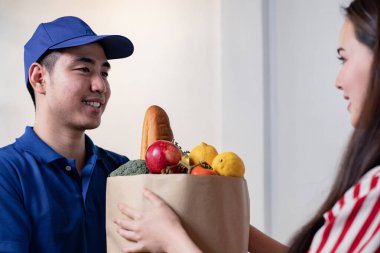 Teslimatçı, hızlı ve güvenilir servisin evinde dururken genç bir bayana yemek veriyor. Kadın gülümseyerek teslimatçıdan yemek topluyor. Teslimat konsepti.