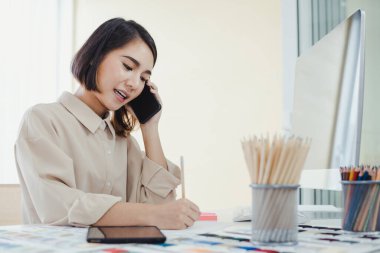 Designer, talking on the phone with the customer and taking note of the work details in order to receive the tailor order for the customer with smile. Startup designer concept.