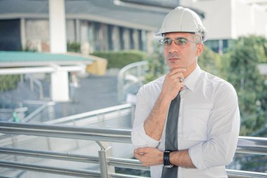 Confident construction engineer in hard hat looking at construction projects. Senior engineer with looking to construction site. Senior engineer wearing protective helmet.