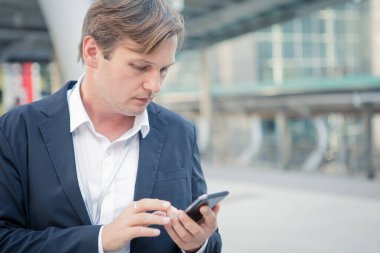 Professional businessman using smartphone outside office building. Handsome businessman in suit holding smartphone in the city