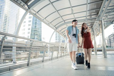 Young couple with dragging a suitcase and talking happily with smiling while to travel in the city. Happiness of young man and young woman in traveling travel together. Travelling concept.