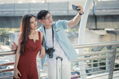 Şehirde seyahat ederken gülümseyen genç bir çiftin akıllı telefonuyla selfie. Birlikte seyahat eden genç bir adam ve genç bir kadının mutluluğu. Seyahat konsepti.