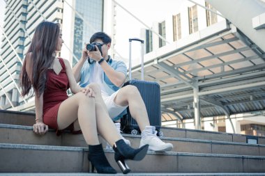 Young man shot his girlfriend while sitting on stairs while happily traveling together. Couple traveller taking photo in the city. Travelling concept.
