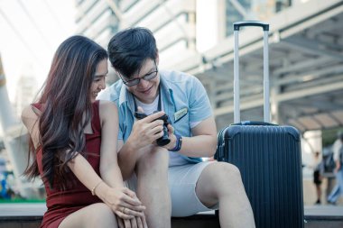 Smiling couple is looking at their photos on the screen of their camera in the city. Travelling concept.