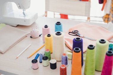 Profesyonel bir moda tasarımcısının iş yerinde. Tasarımcının masasında, elbise dikmek ve kesmek için kullanılan birçok aksesuar var. Modern giysiler tasarlamak için kullanılan ekipmanlı dikiş makinesi.