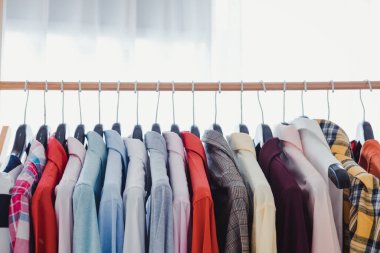 Variety and modern fashion clothes, orderly hanging on the clothesline. Clothes hang on shelf in a designer clothes store. Row of clothes hanging on rack. Fashion trend concept.