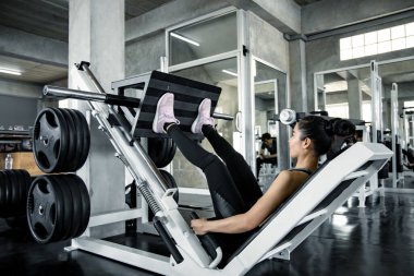 Modern spor salonunda, bacaklarıyla egzersiz makinesinde ağırlıkla oynayan Asyalı seksi kadın. Spor salonunda spor. Egzersiz yaparak sağlığına dikkat et. Vücut geliştirme konseptiyle sağlıklı bakım.