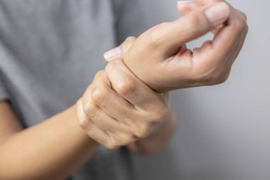 Bilek ağrısı çeken bir kadın. Kadın bileğinde ağrı. Acı dolu bileğini arka planda tutan genç bir kadın..