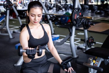 Modern spor salonunda dambılla egzersiz yapan genç bir kadın..