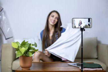 Evde cep telefonuyla internetten kıyafet satan genç bir kadın. İnternetten bir şeyler sat. Canlı satış.