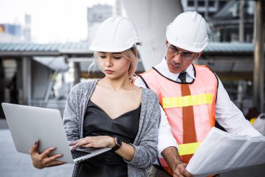 Male and female industrial engineers planning on blueprint and laptop at work site.