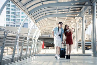 Young couple with dragging a suitcase and talking happily with smiling while to travel in the city. Happiness of young man and young woman in traveling travel together. Travelling concept.