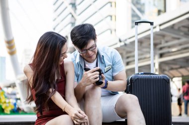 Asian young couple making a reservation look at the camera screen to see the picture after taking the picture while touring the city with happy.