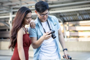 Asian young couple making a reservation look at the camera screen to see the picture after taking the picture while touring the city with happy.