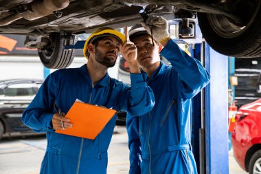 Two mechanic was checking the car suspension. Vehicle raised on lift at maintenance station. Car mechanic working at automotive service center.