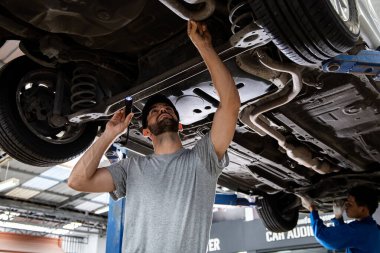 İki tamirci arabanın süspansiyonunu kontrol ediyordu. Araç bakım istasyonunda kaldırıldı. Benzin istasyonunda iki adam var. Otomotiv servisinde çalışan araba tamircisi..