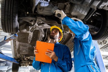 Two mechanic was checking the car suspension. Vehicle raised on lift at maintenance station. Car mechanic working at automotive service center.