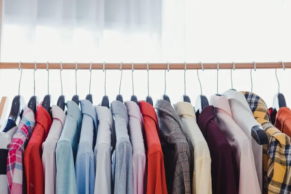 Variety and modern fashion clothes, orderly hanging on the clothesline. Clothes hang on shelf in a designer clothes store. Row of clothes hanging on rack. Fashion trend concept.