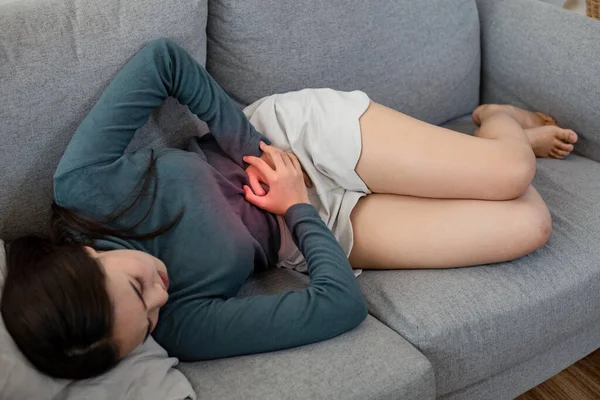 Kanepede karın ağrısı çeken bir kadın. Adet nedeniyle karın ağrısı çeken genç bir kadın. Mide iltihabına bağlı karın ağrısı..
