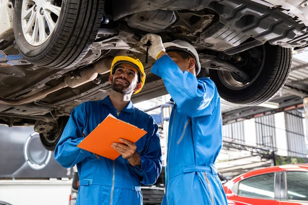 Two mechanic was checking the car suspension. Vehicle raised on lift at maintenance station. Car mechanic working at automotive service center.