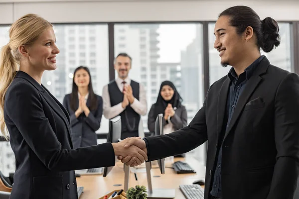 Success work concept, handshake of a male and female office worker in front of the office with smile and happy colleagues in the background.