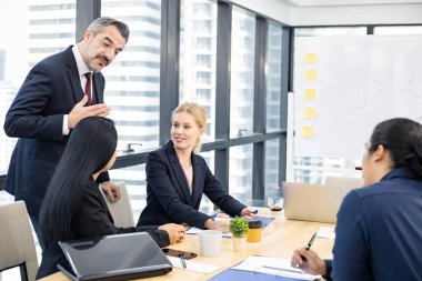 Businessman explaining new business ideas to peers in conference room during meeting at office.