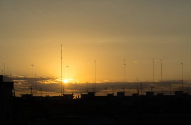 Gün batımında binaların siluetleri antenler ve kablolar ile şehrin silueti
