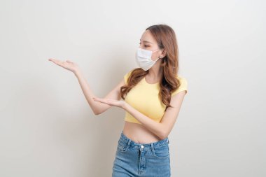 Maskeli güzel bir Asyalı kadın portresi. Beyaz arka planda el sallıyor ya da işaret ediyor.