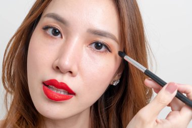 Beyaz arka planda makyaj fırçası olan güzel Asyalı kadın portresi.