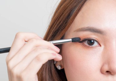 Beyaz arka planda makyaj fırçası olan güzel Asyalı kadın portresi.