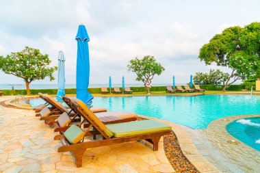 Sandalye havuzu ve şemsiyeyle okyanus arka planında yüzme havuzu