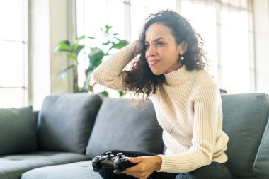Laitin denen kadın evdeki kanepede elinde joystick ile video oyunları oynuyor.