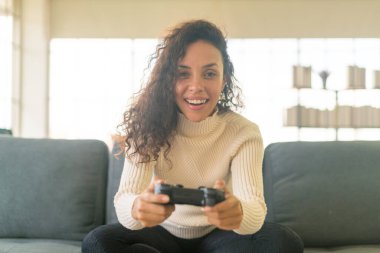 Laitin denen kadın evdeki kanepede elinde joystick ile video oyunları oynuyor.