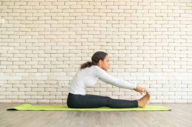Latin kadın beyaz tuğlalı minder üzerinde yoga yapıyor.