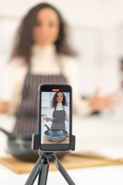 Latin kadın blogda paylaşmak için mutfakta video ve yemek çekiyor.