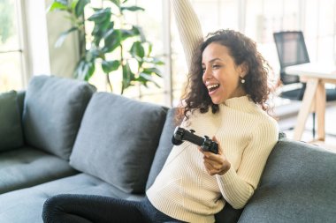 Laitin denen kadın evdeki kanepede elinde joystick ile video oyunları oynuyor.