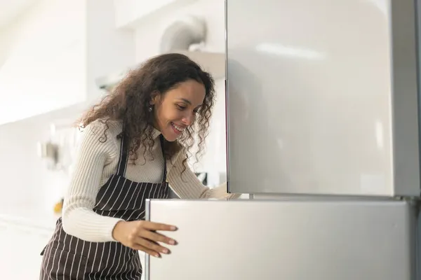 Latin woman open fridge or refrigerator in kitchen