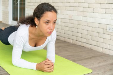 Latin kadın beyaz tuğlalı minder üzerinde yoga yapıyor.