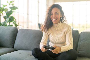 Laitin denen kadın evdeki kanepede elinde joystick ile video oyunları oynuyor.