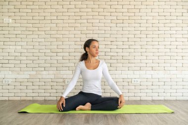 Latin kadın beyaz tuğlalı minder üzerinde yoga yapıyor.