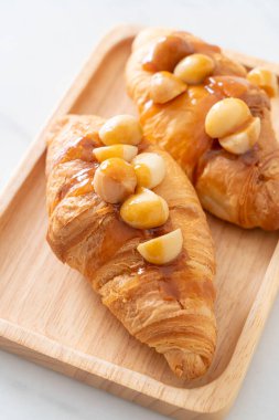 Macadamia ve ahşap tabakta karamel ile kruvasan.