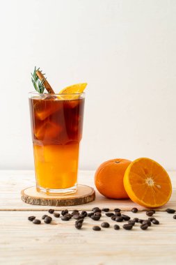 Bir bardak buzlu americano sade kahve ve ahşap arka planda biberiye ve tarçınla süslenmiş portakal ve limon suyu.