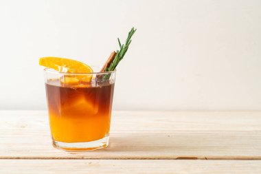 Bir bardak buzlu americano sade kahve ve ahşap arka planda biberiye ve tarçınla süslenmiş portakal ve limon suyu.