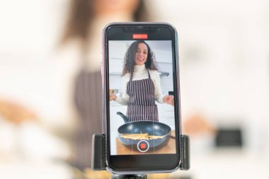 Latin kadın blogda paylaşmak için mutfakta video ve yemek çekiyor.